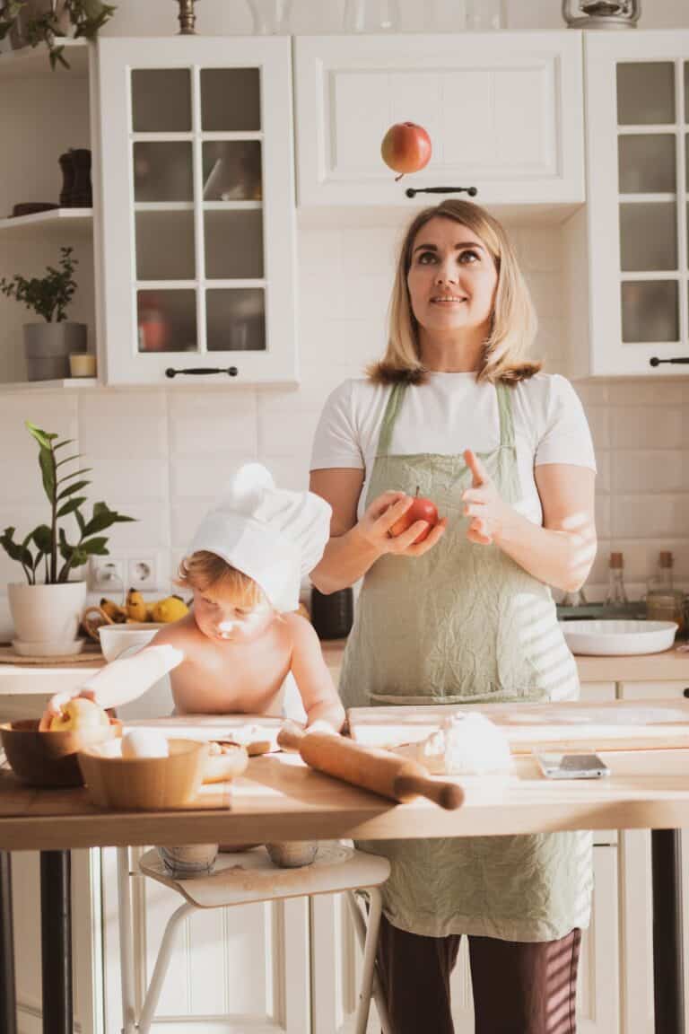 Pretty young woman in and her little son are preparing pie at home in kitchen and she juggles apples